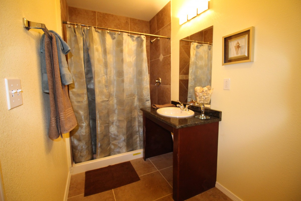 A well-lit bathroom featuring a shower with a curtain, a sink with a vanity, and neatly hung towels.