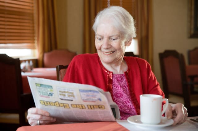 An elderly woman enjoying a newspaper with a cup of coffee indoors.