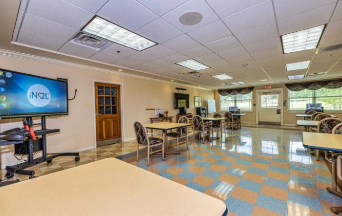 A spacious room with tables and chairs, featuring large windows and ceiling lights.