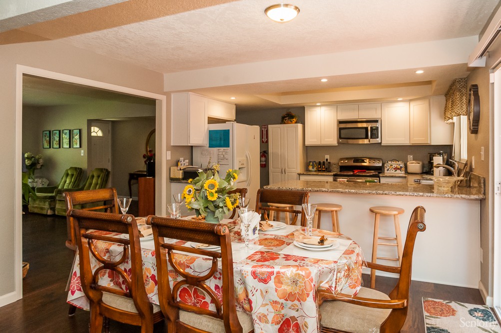 A cozy kitchen and dining area with a floral tablecloth and wooden chairs.