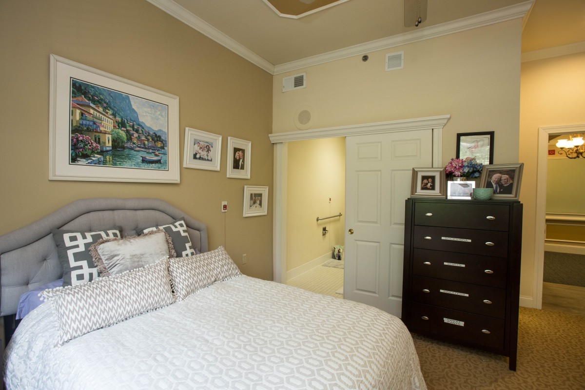 A cozy bedroom with a neatly made bed, artwork on the walls, and a dark wooden dresser.