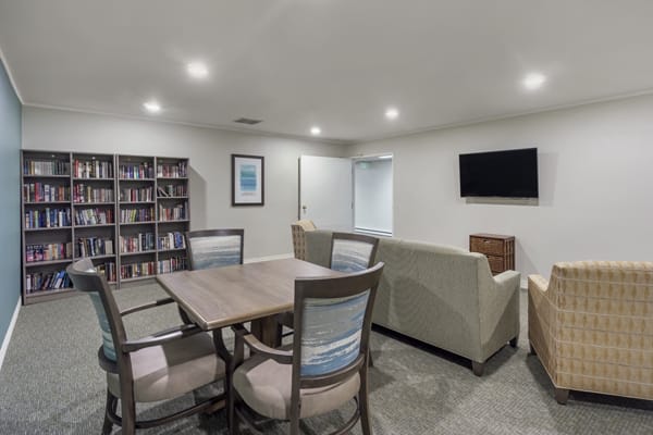 A cozy living area with a table and chairs, a sofa facing a TV, and a wall bookshelf.