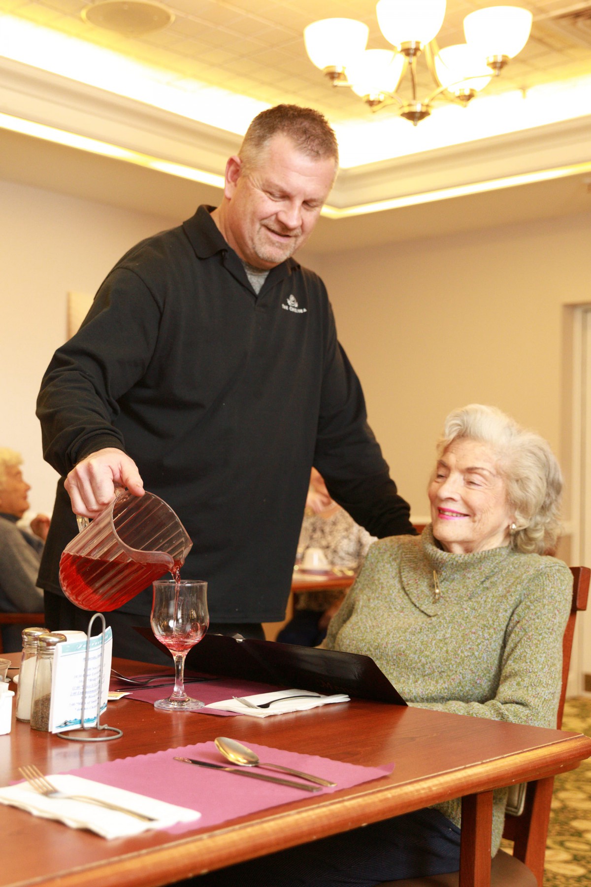 A man is pouring a drink for an elderly woman in a restaurant setting.