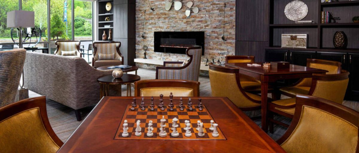 A cozy living room featuring a chessboard ready for play, with comfortable seating and a stone fireplace.