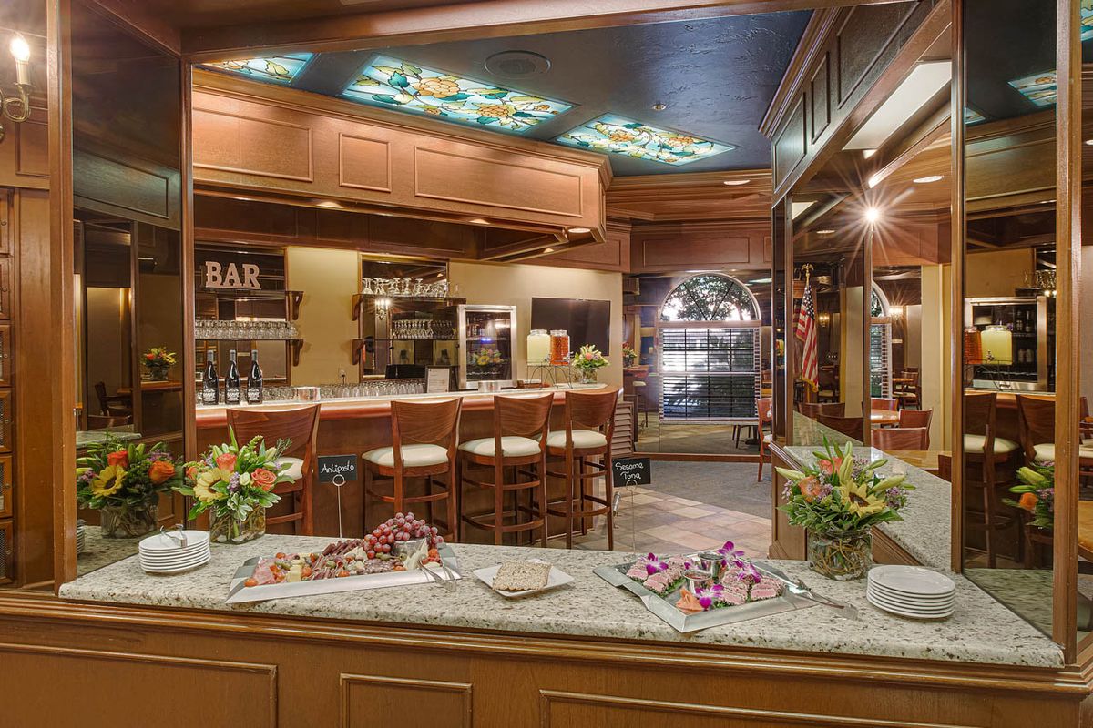 A cozy and elegantly decorated bar with a marble countertop, surrounded by wooden chairs and floral arrangements.