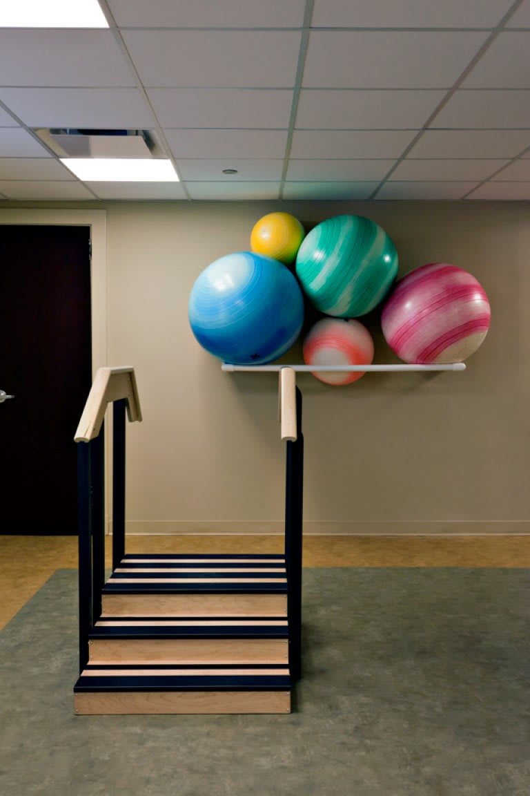 A set of colorful exercise balls stacked on a shelf in a fitness or rehabilitation center.