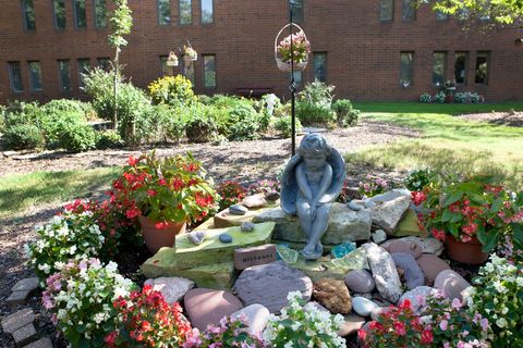 A serene garden setting featuring a thoughtful statue surrounded by vibrant flowers and decorative rocks.