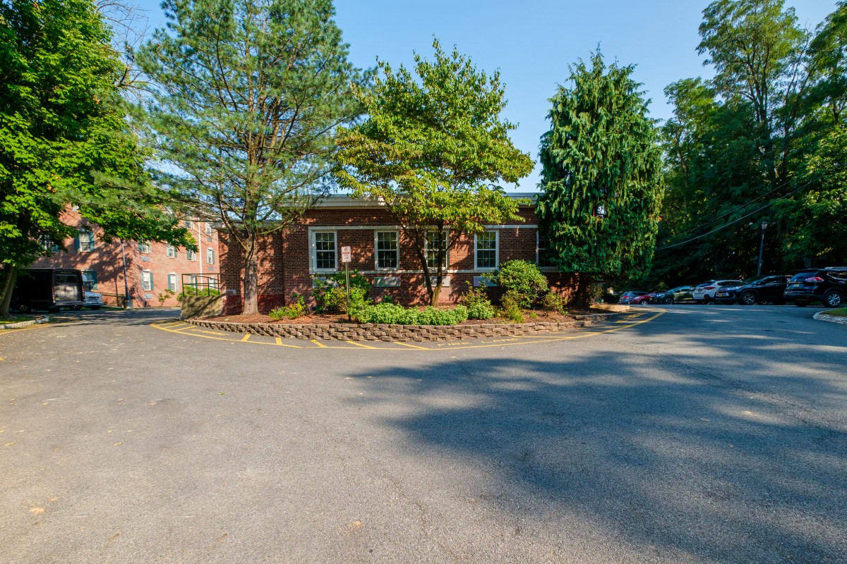 A brick house surrounded by trees and landscaping with a driveway in a suburban setting.