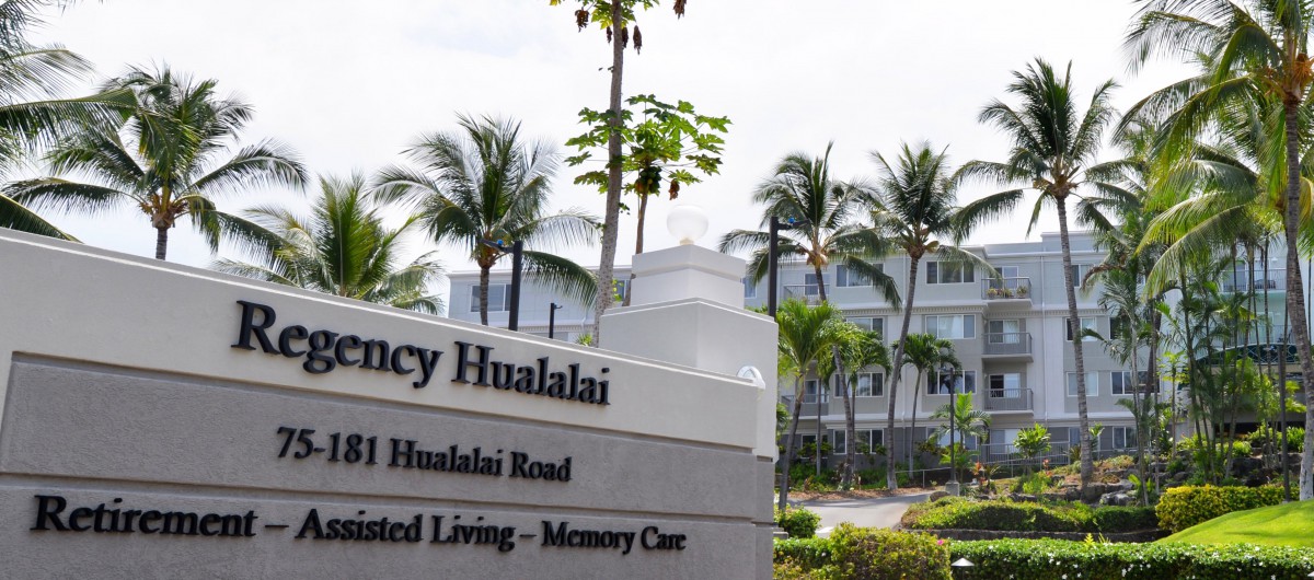 Entrance sign for Regency Hualalai, an assisted living and memory care facility surrounded by palm trees.