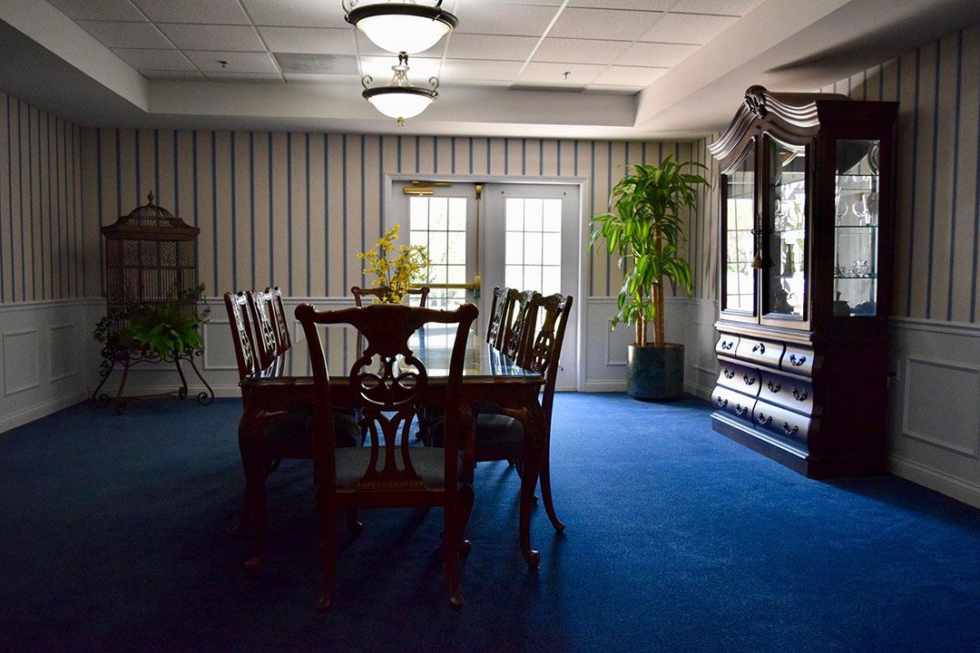 A traditional dining room with a wooden table and chairs, complemented by indoor plants and a mirror.