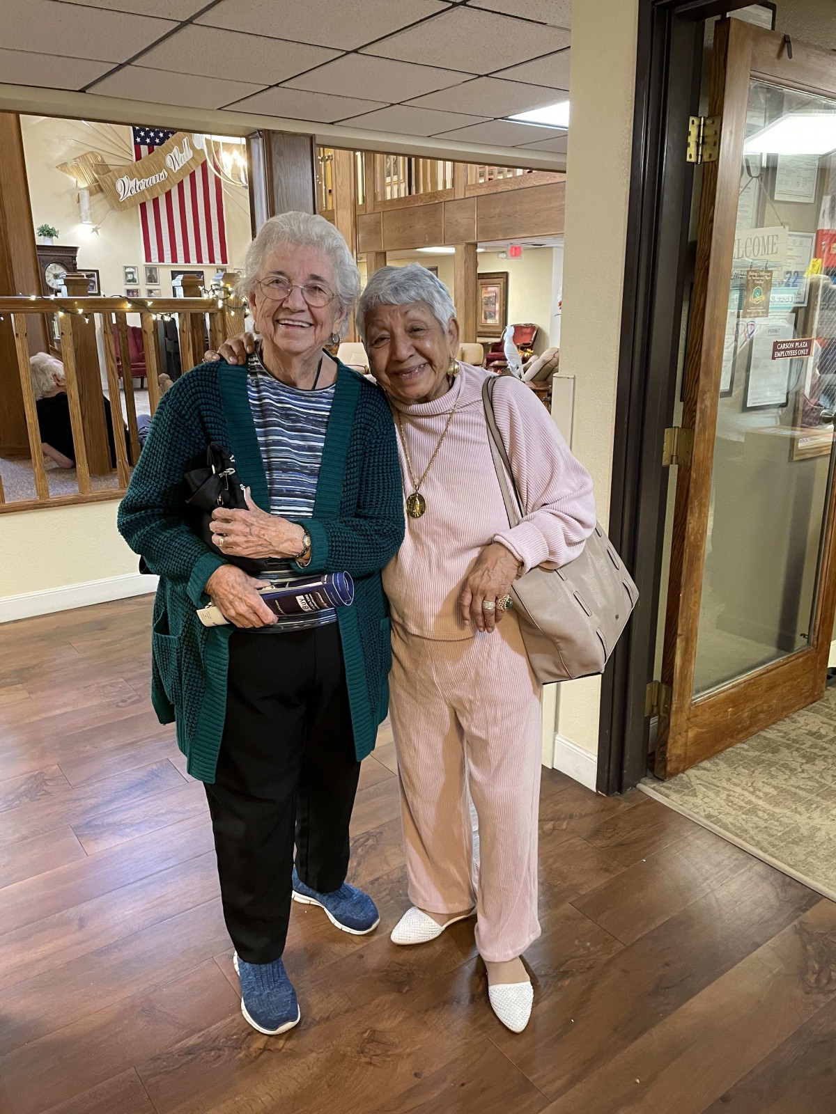 Two elderly friends smiling and posing together indoors.