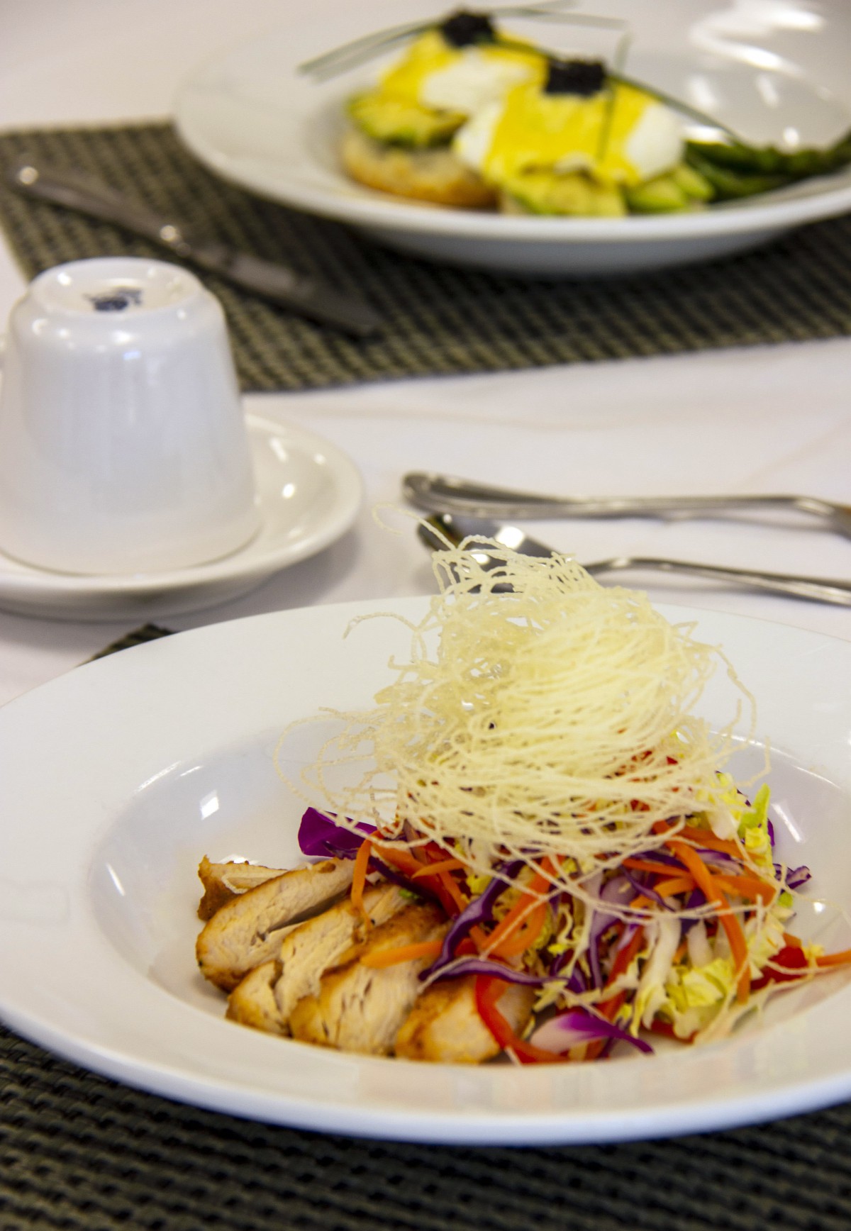 A gourmet chicken salad with colorful vegetables and garnish served on a dining table.