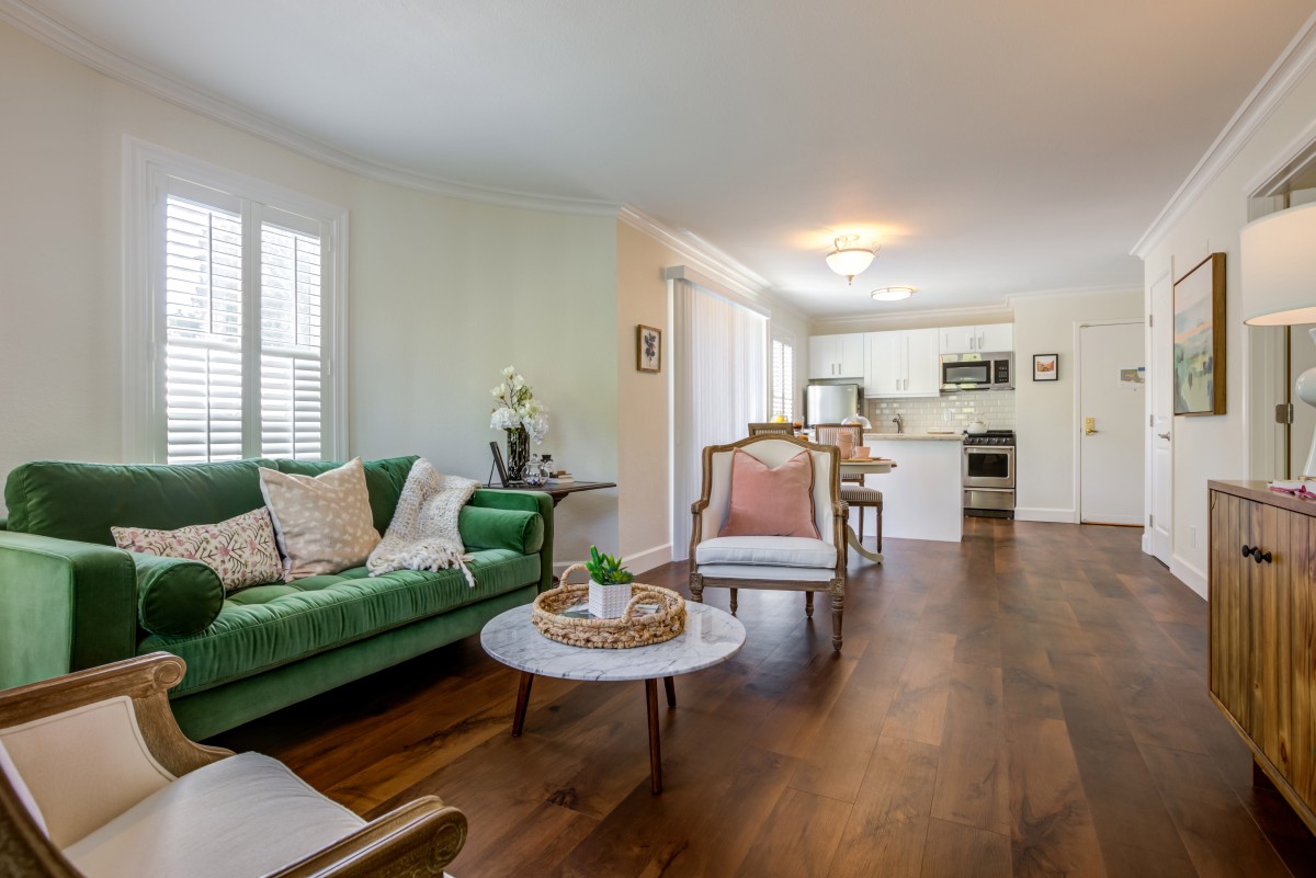 A modern open-plan living room with a green sofa and wood flooring.