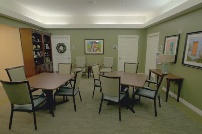 A conference room with tables and chairs arranged for a meeting, featuring a bookcase and artwork on the walls.