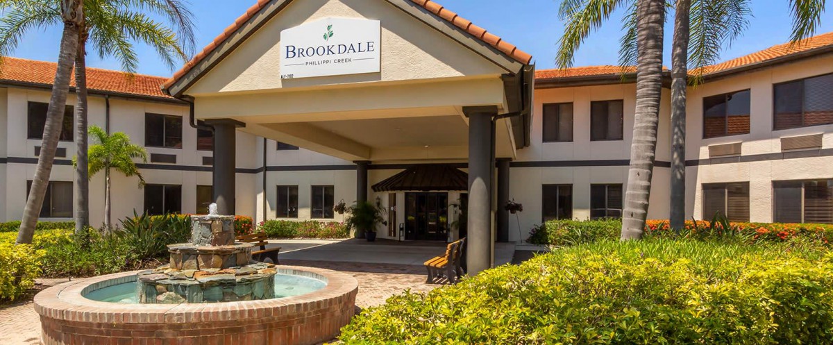 The front entrance of a Brookdale building with landscaping and a fountain.