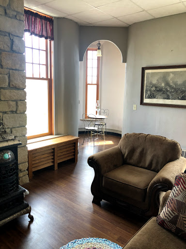 A cozy living room featuring a comfortable armchair, a stone fireplace, and large windows that allow ample natural light.