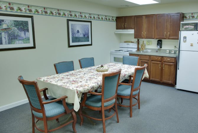 A cozy kitchen with a dining table and chairs, featuring wood cabinets and a patterned tablecloth.