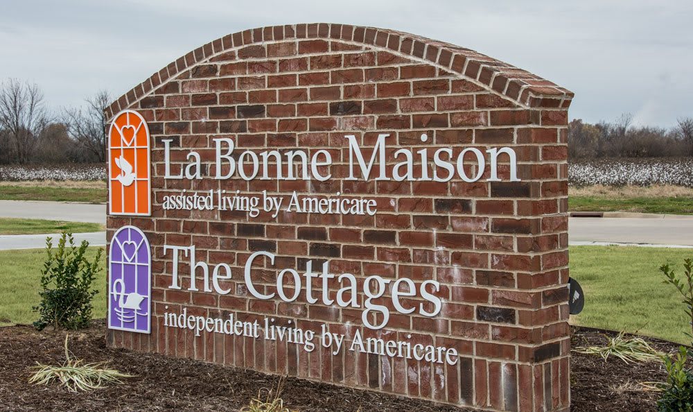 A brick sign displaying 'La Bonne Maison' for assisted living and 'The Cottages' for independent living.