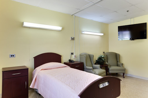 A hospital room featuring a bed with a pink cover and two chairs.