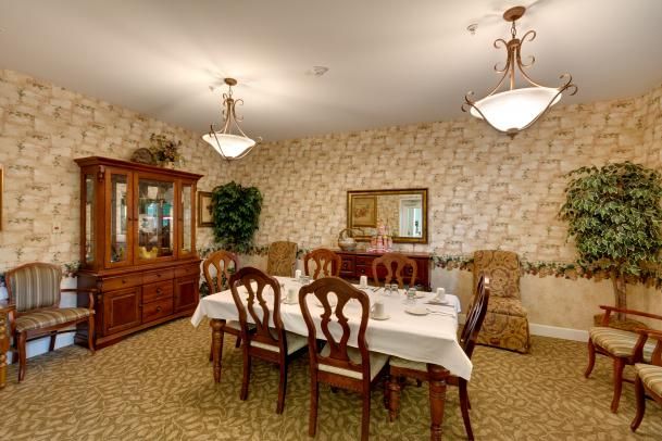 A classic dining room setup featuring a table with chairs, chandeliers, and a wooden cabinet against a decorated wall.