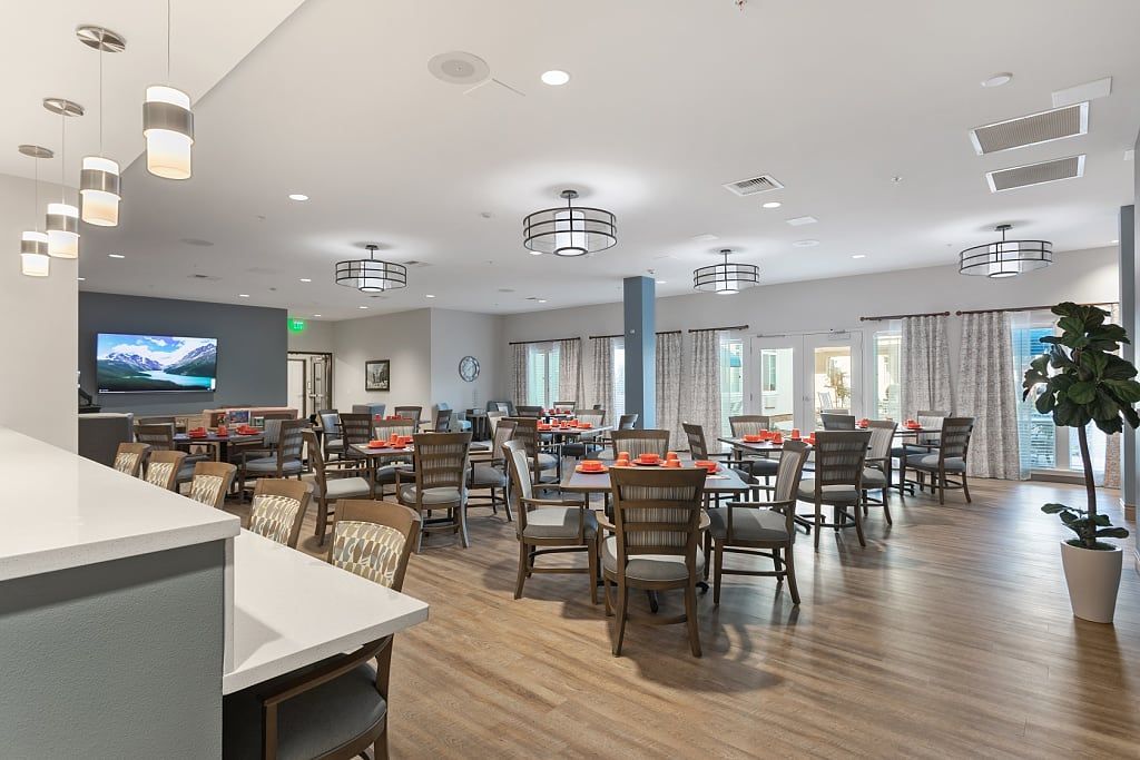 A spacious and modern dining room with multiple tables and chairs, featuring stylish light fixtures and large windows.