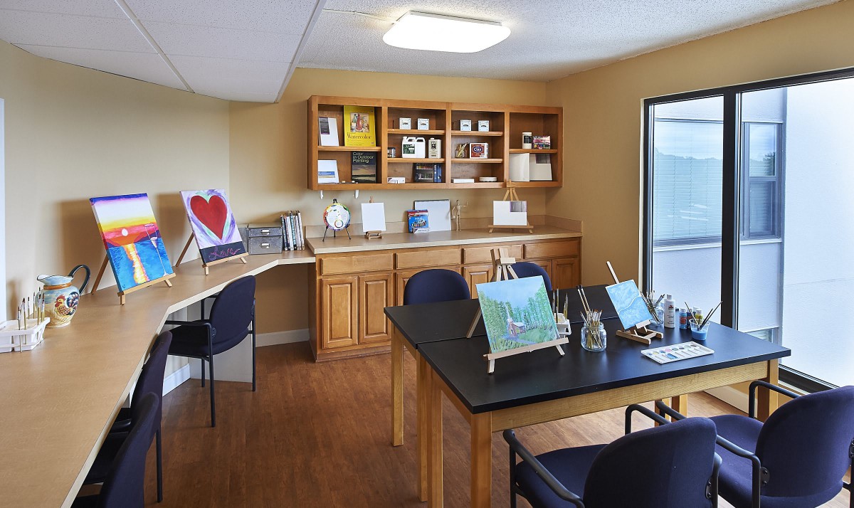 A classroom or study area featuring desks, chairs, wooden cabinets, and artwork displays.