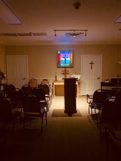 A small chapel interior with a pulpit, seating, and a stained glass window.