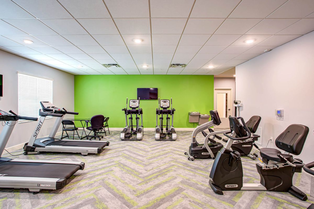 A modern gym with various exercise equipment, including treadmills and stationary bikes, against a vibrant green accent wall.