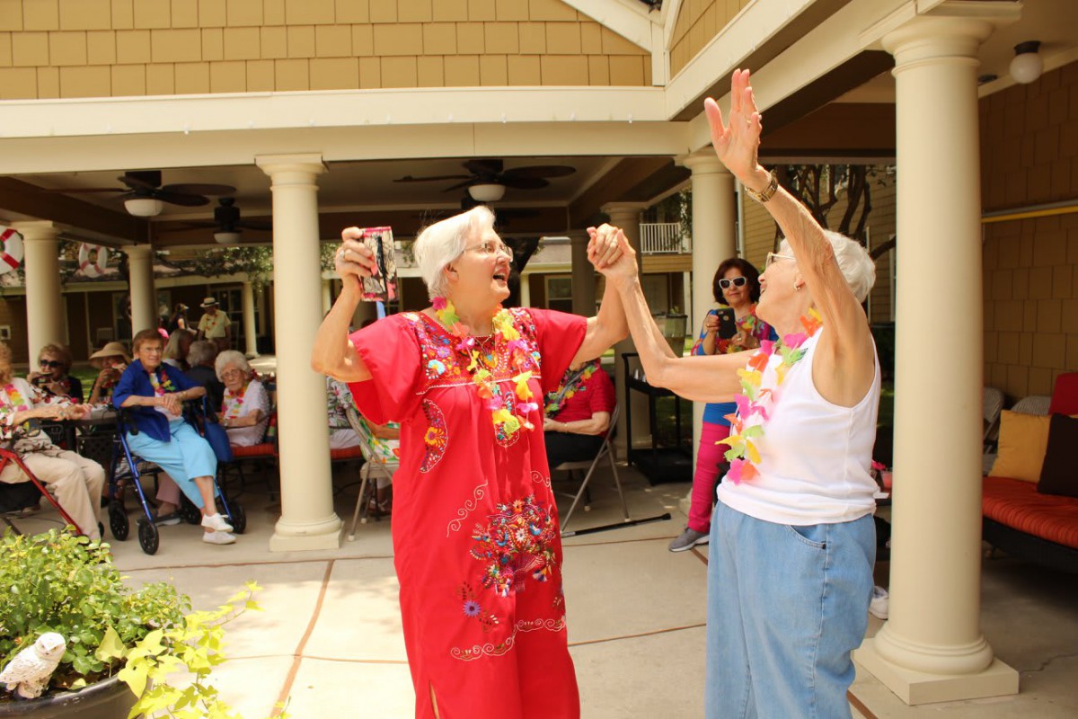 Two senior women joyfully dancing together at an outdoor celebration.