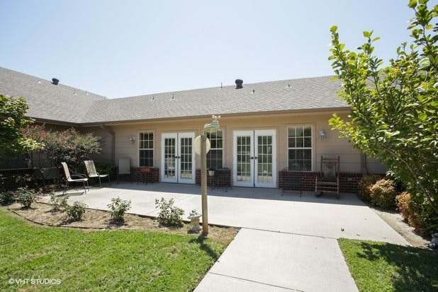 A patio area in front of a building with multiple windows and a well-maintained garden.
