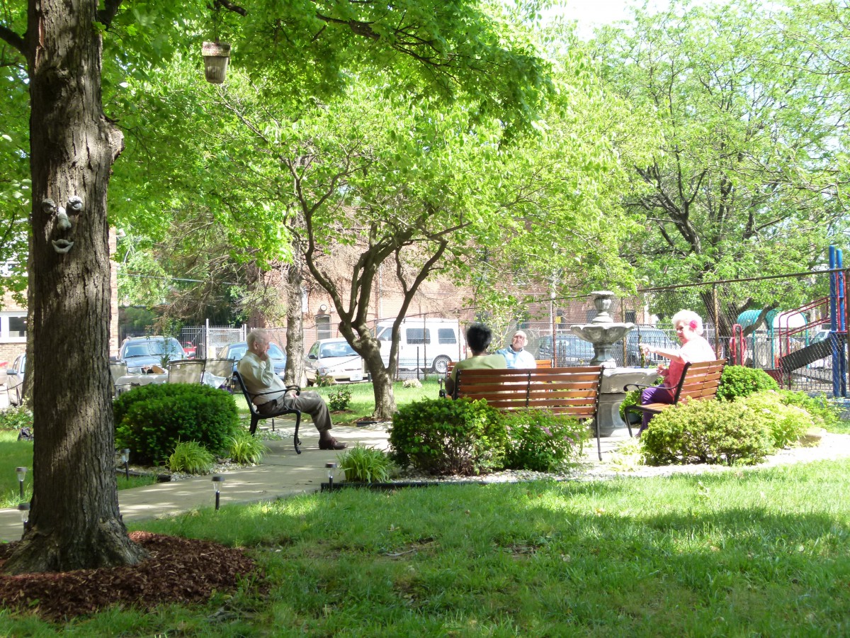 A serene park scene with people sitting on benches surrounded by lush greenery and trees.
