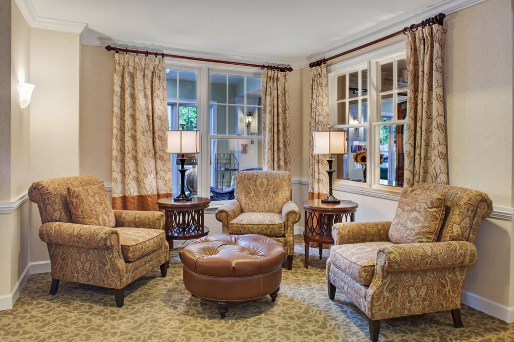 A cozy living room featuring armchairs, an ottoman, and elegant lighting.