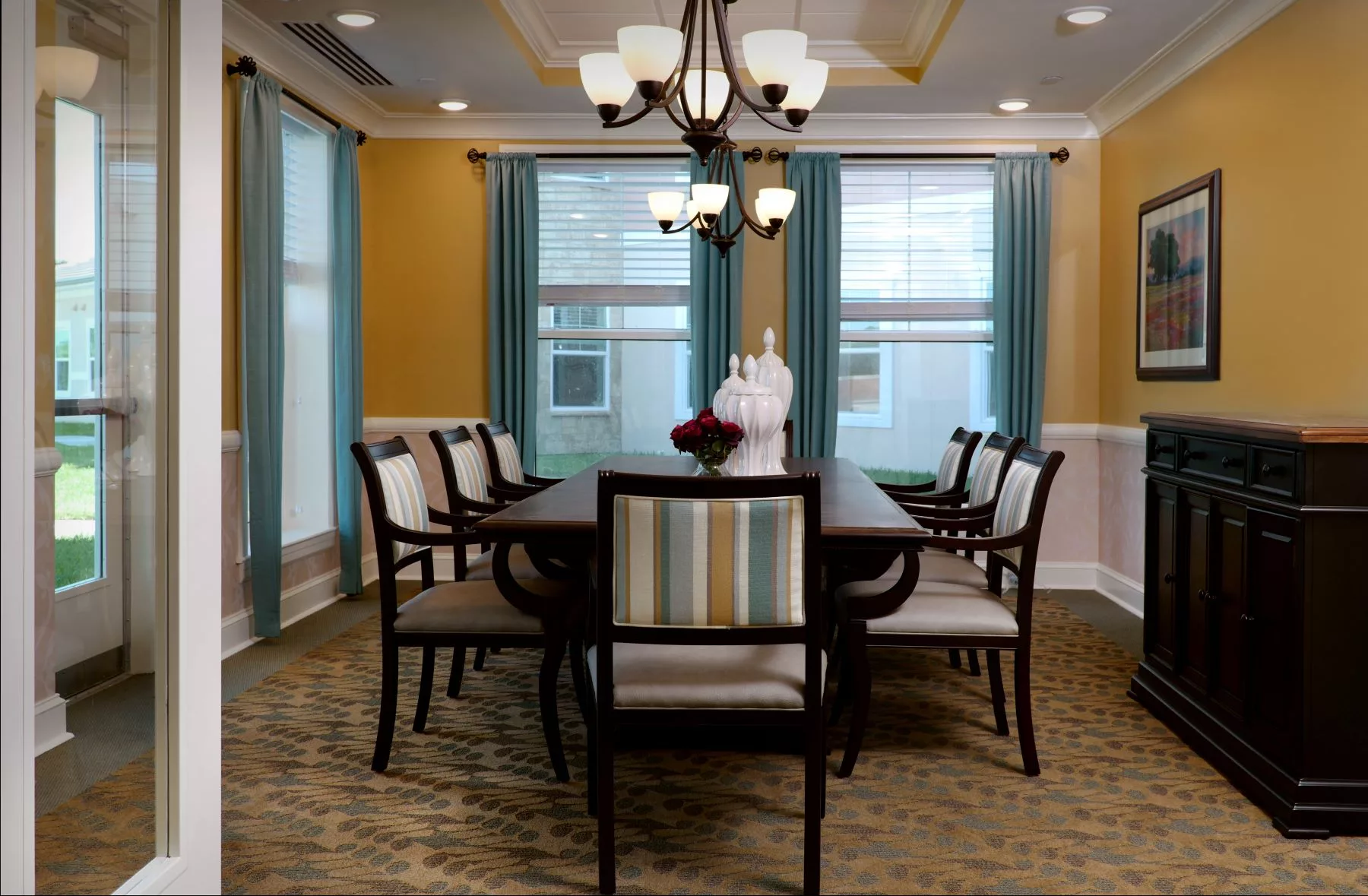 A well-furnished dining room with a large table, surrounded by chairs, under an elegant chandelier.