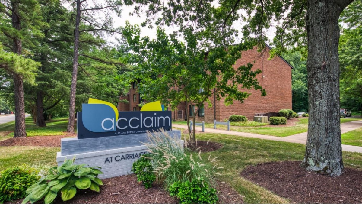 A landscaped entryway with a sign for 'acclaim' at an apartment complex.
