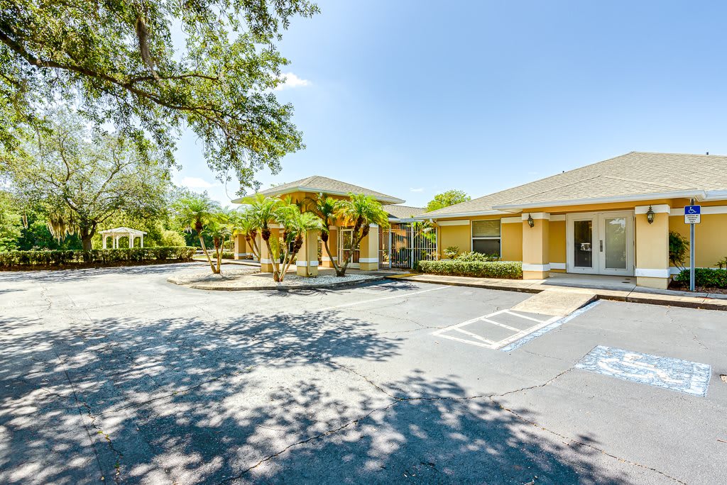 A sunny view of a building with a parking lot and surrounding trees.