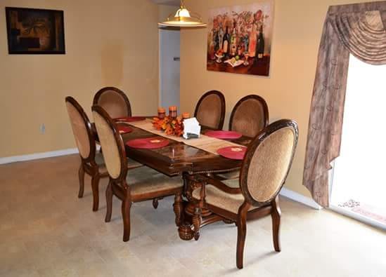 A classic dining room with a wooden table and upholstered chairs, decorated with a central runner and artwork on the wall.