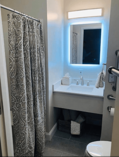 A modern bathroom with a well-lit mirror and shower curtain.