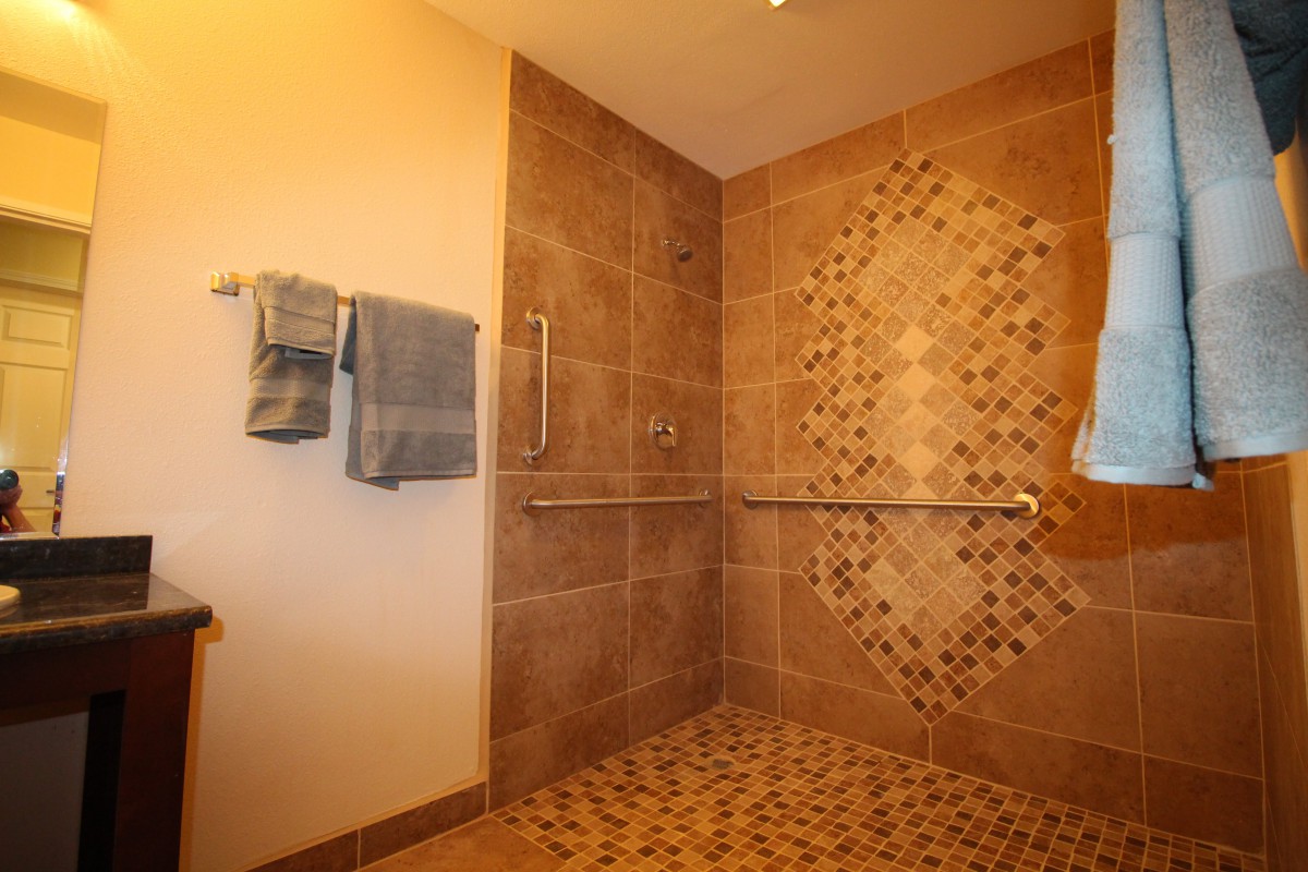 A modern walk-in shower with tiled walls and a handrail.