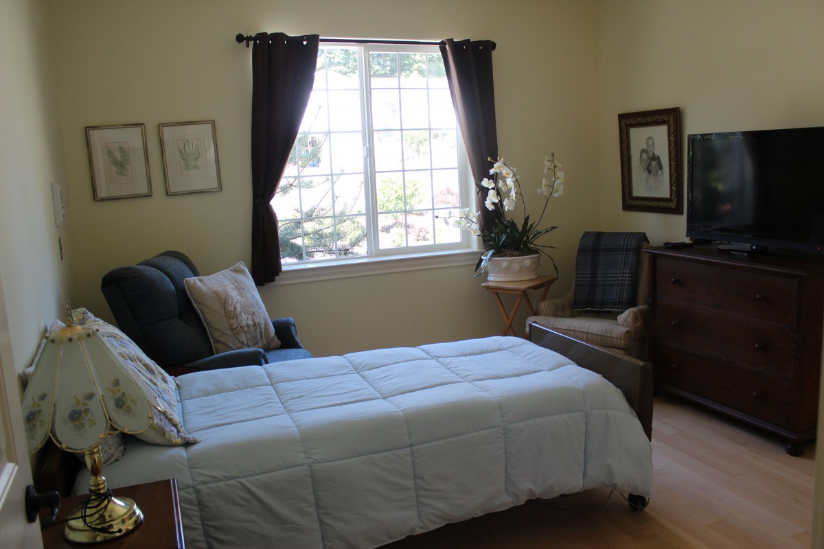 A cozy bedroom with a bed, armchair, and window featuring dark curtains.