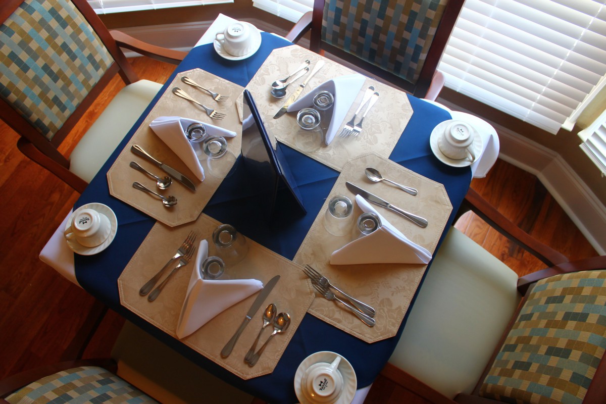A formal dining table set for four with elegant napkin folds and complete place settings.