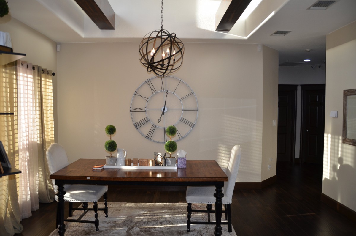 A modern dining room with a wooden table, unique chandelier, and decorative wall clock.