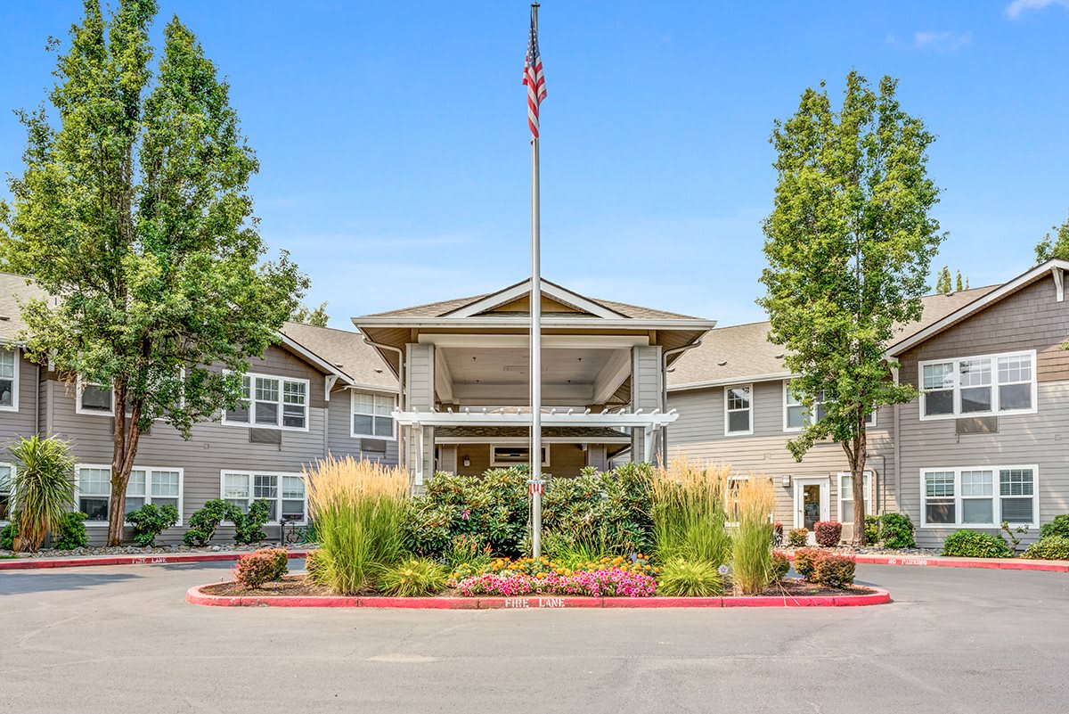 A well-maintained building entrance with a flagpole, surrounded by lush landscaping and trees.