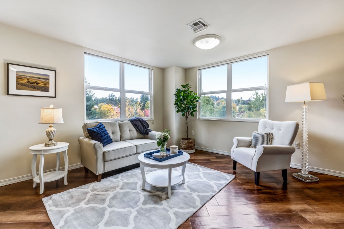 A bright and cozy living room with a sofa, armchair, and coffee table, featuring large windows and hardwood flooring.