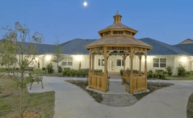 A wooden gazebo in front of a building under the evening sky with the moon visible.