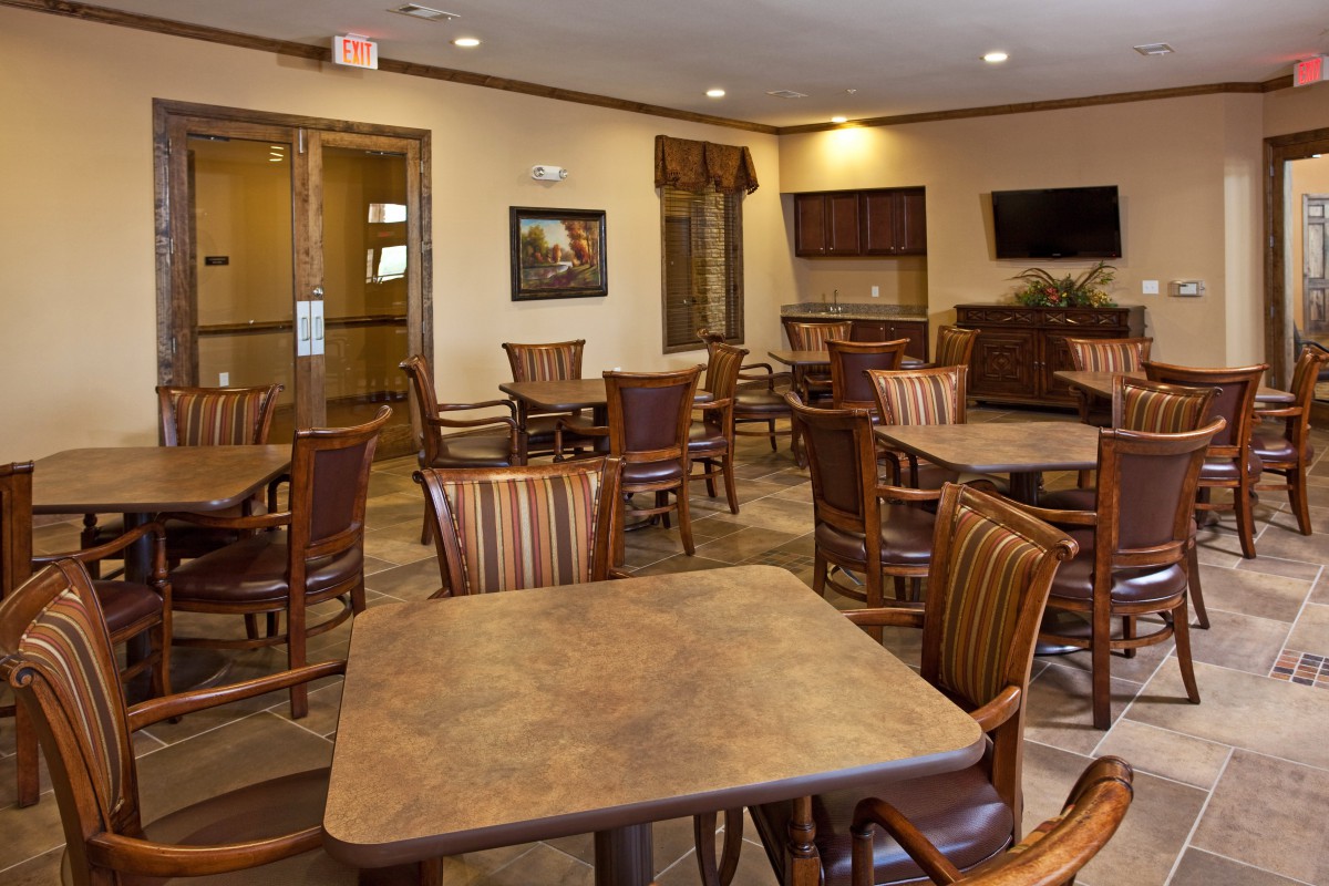 An empty dining area with wooden tables and chairs, featuring a television on the wall.