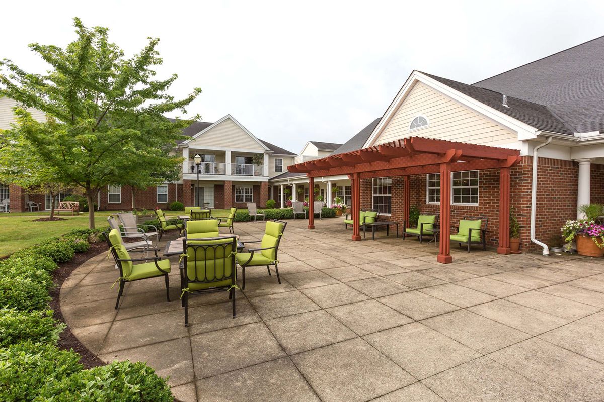 An outdoor patio area with green seating and a pergola, adjacent to residential buildings.