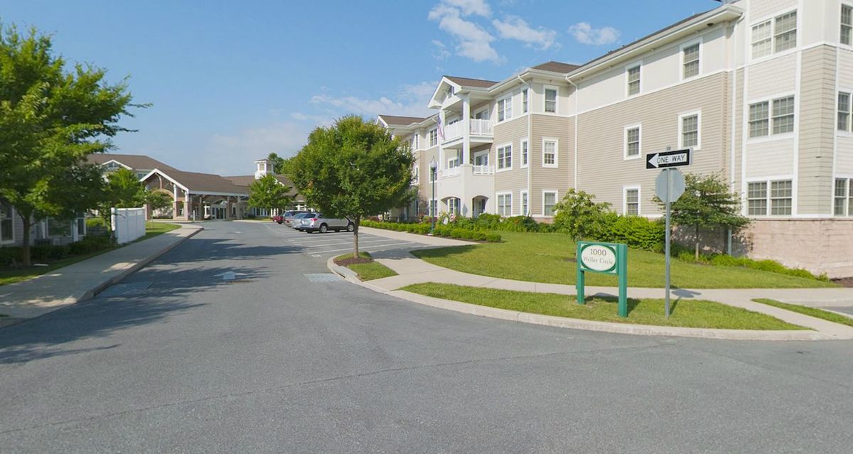 A view of a residential apartment complex with a parking lot and green spaces on a sunny day.