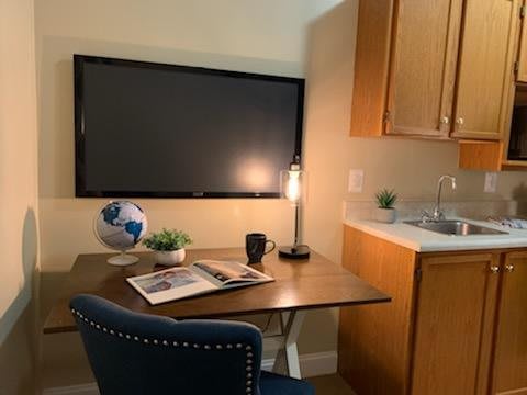 A cozy home office setup with a desk, chair, and various items including a lamp, cup, book, globe, and wall-mounted TV.