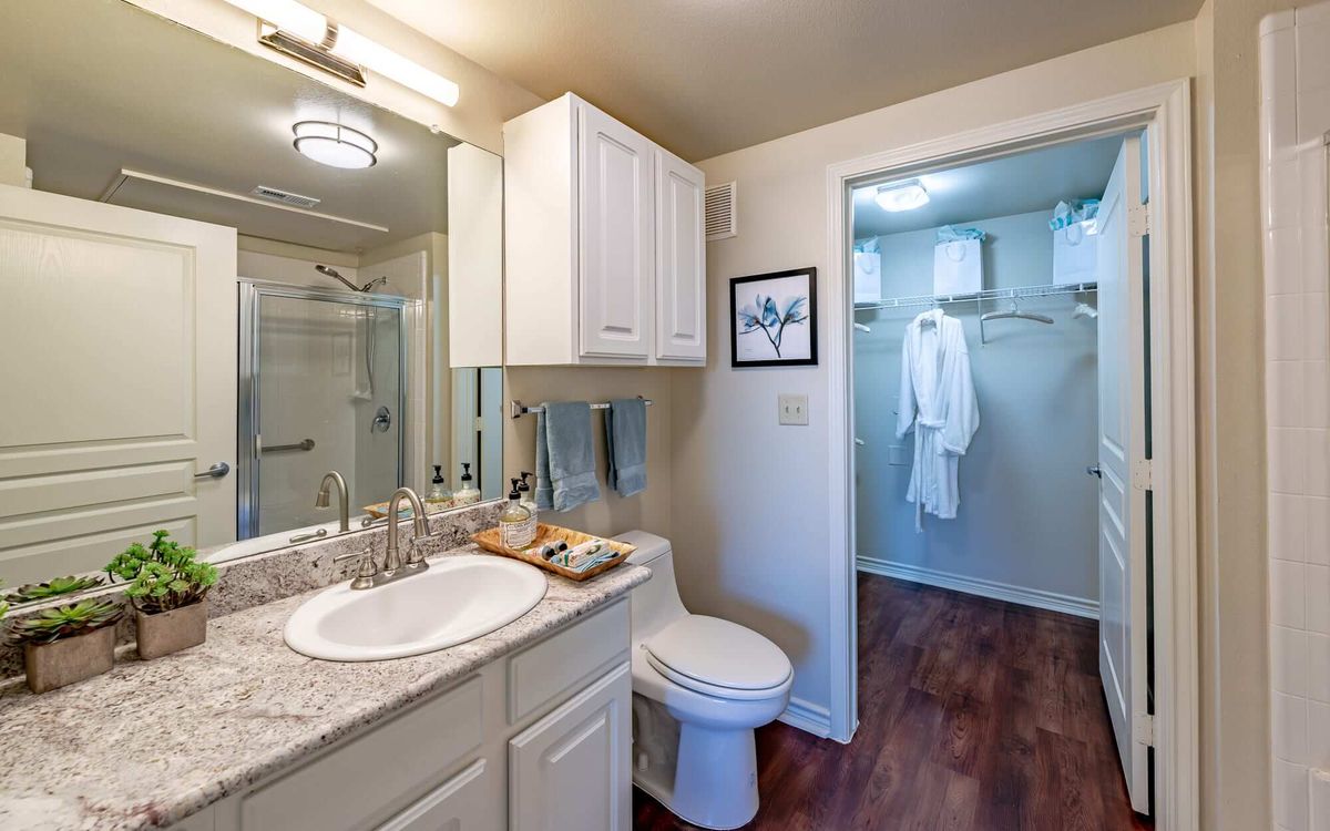 A clean and modern bathroom with a shower, sink, and toilet, featuring wooden floors and white cabinetry.