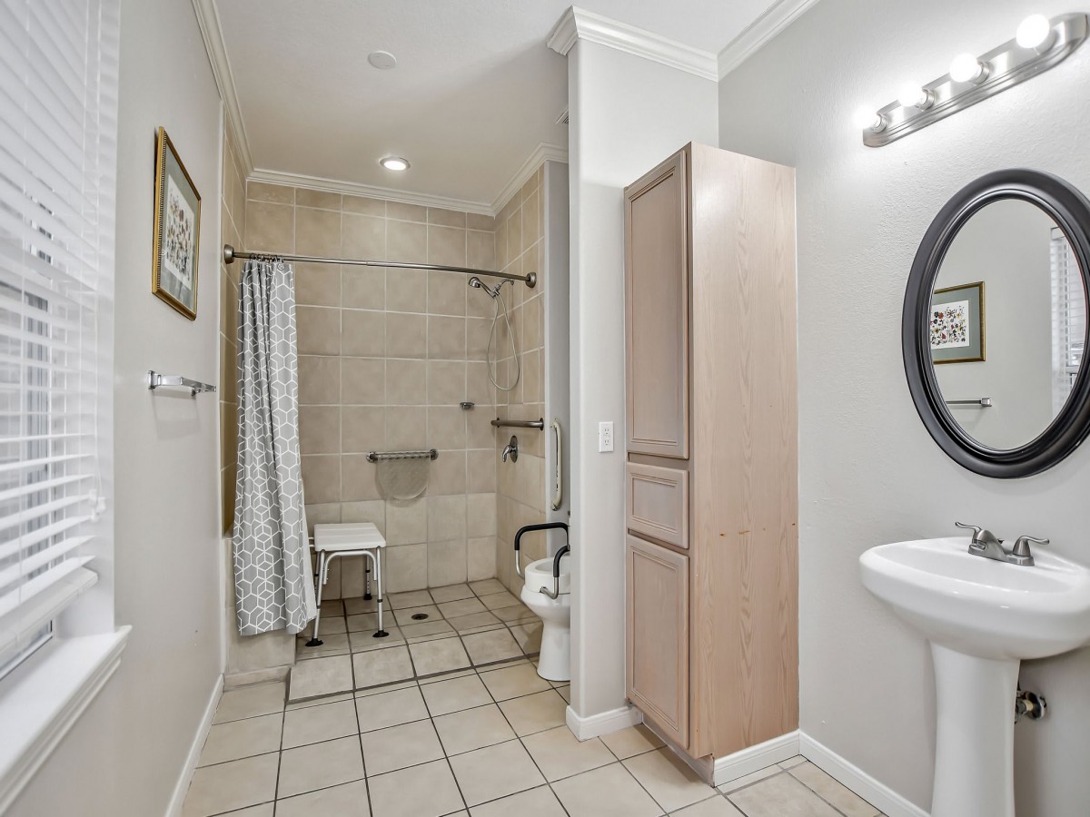 A bathroom with an accessible shower, toilet, sink, and storage cabinet.